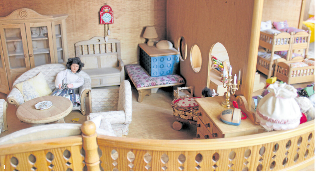 Blick in ein komfortabel eingerichtetes Puppenhaus, mit Kachelofen, bequemen Polstersesseln, Doppelstockbetten und Spielzeug für die vielen Puppenkinder.