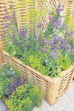 Ein hölzernes Hochbeet in aparter Flechtoptik mit Kräutern.