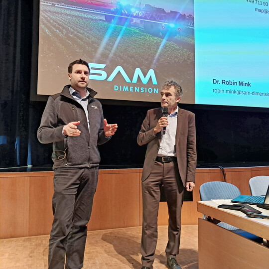 Dr. Robin Mink erklärt, wie sein Start-up SAM-DIMENSION über Befliegen der Felder mit Drohnen Karten zum Unkrautbefall erstellen kann. Rechts Moderator Dr. Wilfried Hermann.