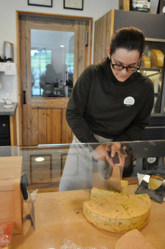 Gekonnt schneidet die junge Frau hinter der Verkaufstheke mit einem Käsemesser für Hartkäse ein Stück vom Käselaib.