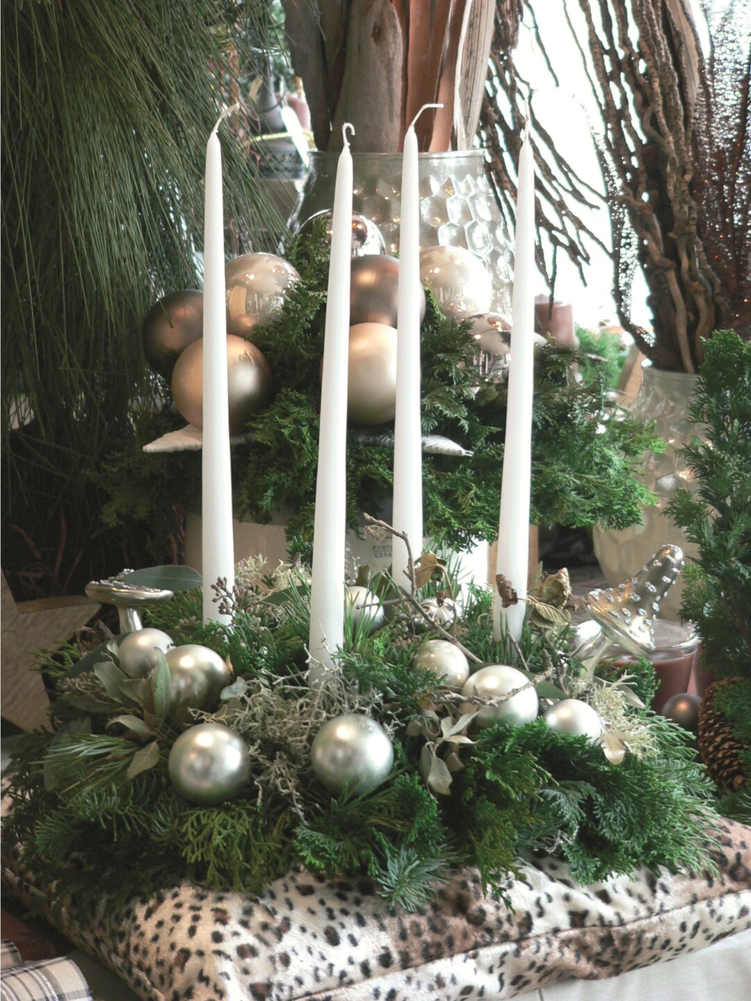 Eine Alternative zum klassischen Adventskranz: Elegante Leuchterkerzen mit dem RAL-Gütezeichen werden mit weihnachtlichen Accessoires auf einem Tannenkranz platziert. Bei diesem Arrangement unbedingt für Standfestigkeit sorgen und zwischen Kranz und Kissen aus Sicherheitsgründen eine Metallunterlage legen. Außerdem: Kerzen nie unbeaufsichtigt brennen lassen.