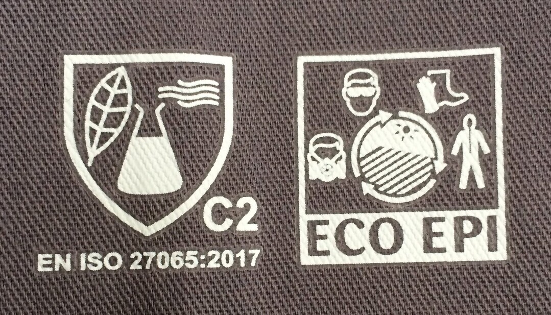 Der Erlenmeyerkolben mit Blatt zeigt an, dass es sich hierbei um Arbeitskleidung handelt, die nach DIN EN ISO 27065 zertifiziert ist.