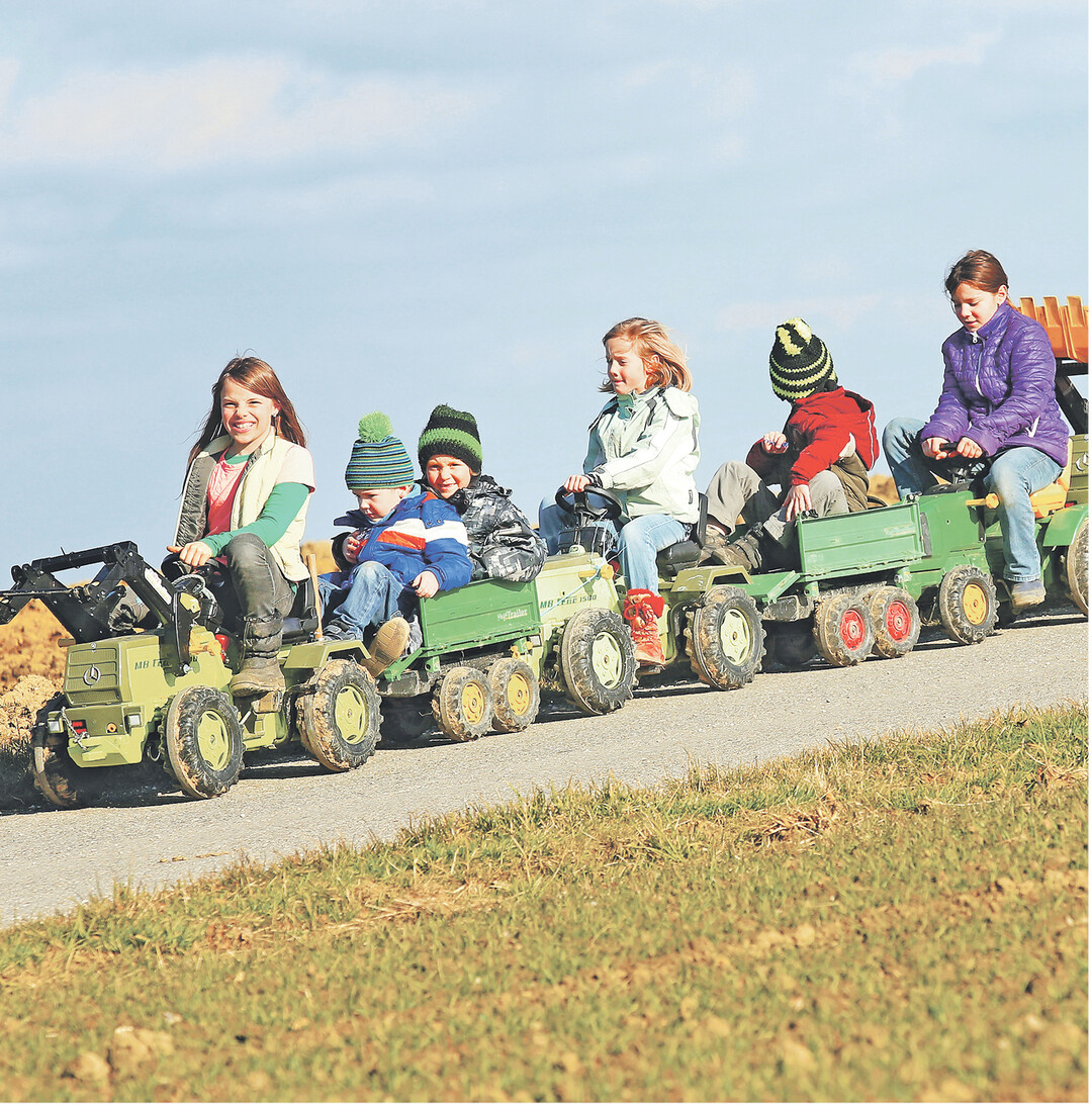 Einen Zug mit insgesamt sechs Fahrzeugen haben diese Kinder in Aderzhofen zusammengespannt und genießen ihre gemeinsame Abfahrt auf einem Feldweg.