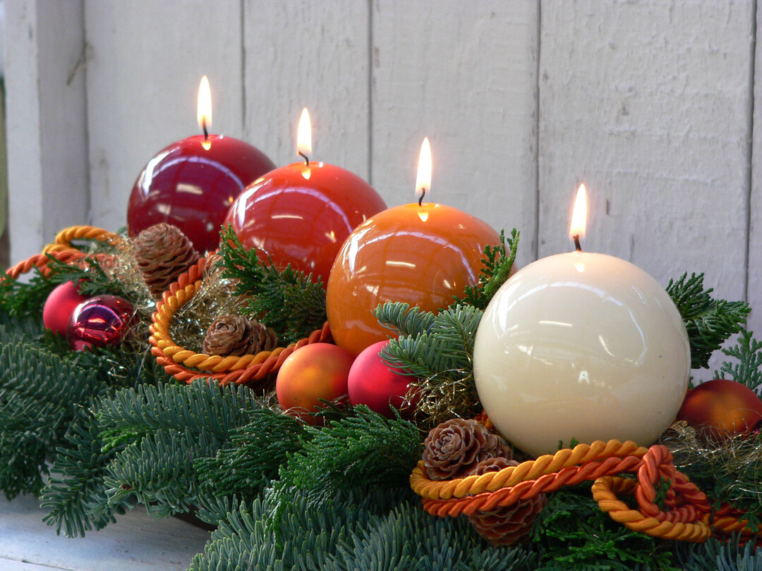 Vier glänzende Kugel-Kerzen in unterschiedlichen Braun- und Rotnuancen werden mit weihnachtlichen Accessoires zu einem Adventsgesteck arrangiert.