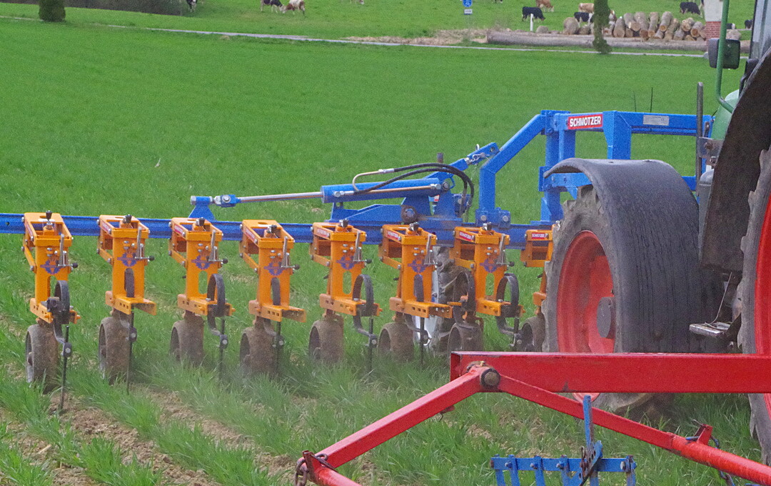 Hacke Schmotzer mit Kombi-Parallelogramm: Die kameragesteuerte Hacke kann laut Hersteller im Front- oder Heckanbau gefahren werden, wobei die Parallelogramme immer ziehend angeordnet sind. Im Einsatz war die betriebseigene Hacke im Frontanbau. Außerdem wurden noch zwei weitere Hackgeräte von Schmotzer ausgestellt. Diese waren mit einem kleinen Kombiparallelogramm und Handsteuerung sowie Kamera ausgestattet. Bei neusten Kamerasystemen setzt der Hersteller unter anderem auf die Erkennung von Blattform und Farbe, was die Sicherheit bei der Erkennung von Kulturen verbessern soll.