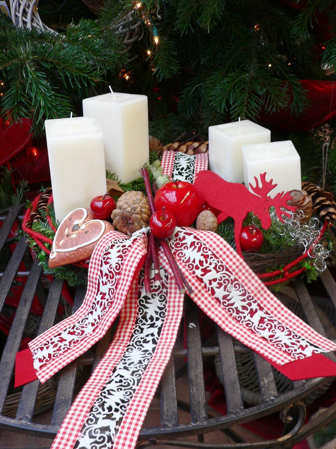 Weiße Quader-Kerzen in RAL-Qualität zaubern in Kombination mit weihnachtlichen Accessoires in rot-weiß einen zauberhaften Adventskranz. Das aufwendig gestaltete Band in Scherenschnittoptik, sowie der kleine Elch aus Filz verleihen dem Arrangement einen Hauch von schwedischer Weihnachtsromantik.