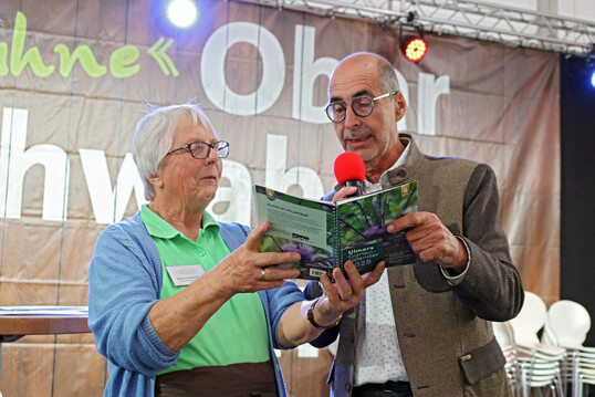 Gemeinsamer Blick in den Ulmer Gartenkalender 2025: Zu jedem Monat gibt es ein tolles Bild. Am 17. Oktober sollten Obstbume und Beerenstrucher gepflanzt werden, rezitierte und beglckwnschte Bernhard Bitterwolf eine der Buch-Gewinnerinnen. 