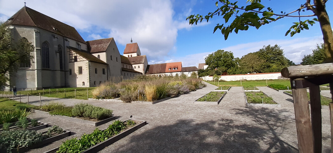 Blick auf das Münster und ehemalige Kloster in Reichenau-Mittelzell, im Mittelalter ein kulturelles Zentrum der damaligen Welt. In rechteckigen Beeten links der Strabo-Kräutergarten, davor der Gemüsegarten und ein Staudenbeet „Blau-Gold“.