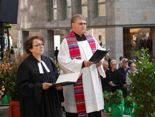 Pfarrerin Monika Renninger und Stadtdekan Oliver Lahl vor der Stiftskirche beim Erntedank-Wochenmarkt in Stuttgart.